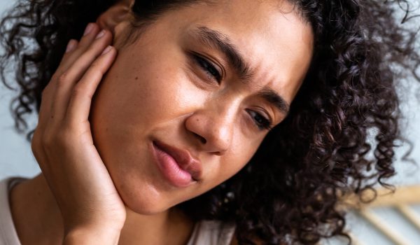 a close up of a woman holding her ear in visible pain